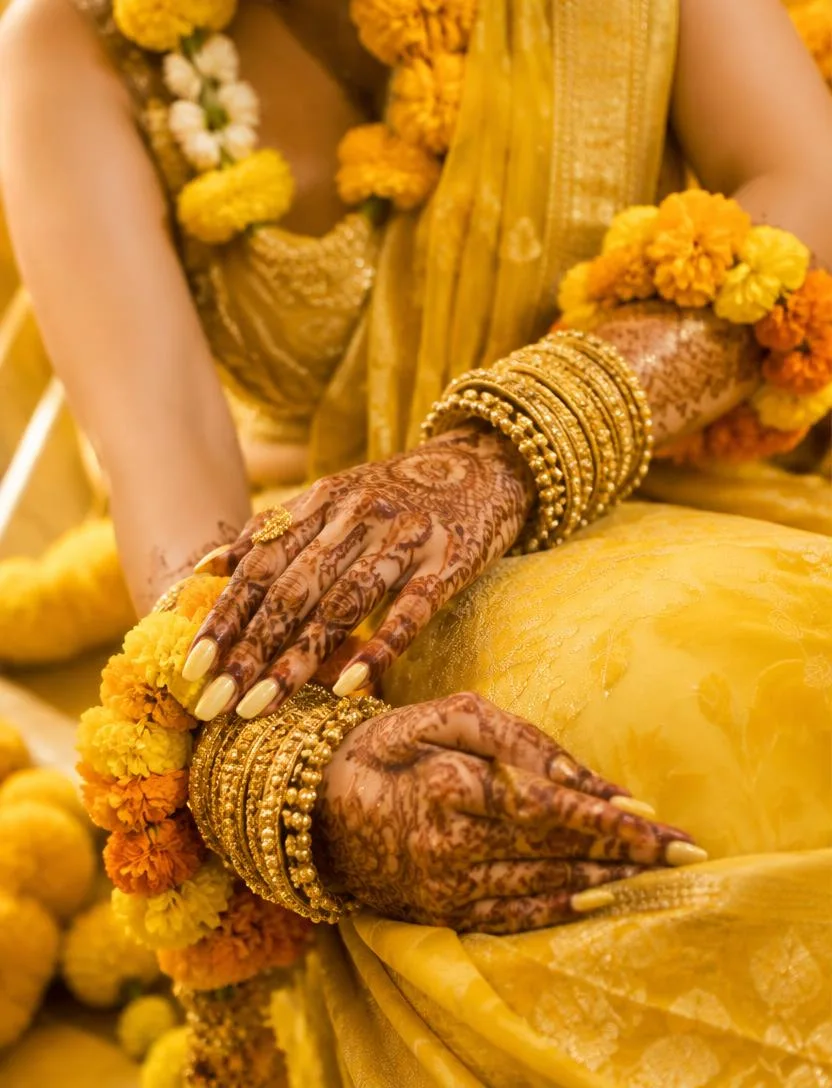 Bride's mehndi hands with gold bangles and marigold garlands at a Gaye Holud